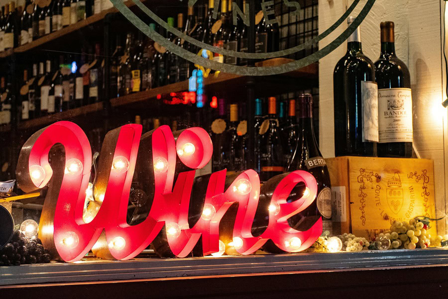 Best Wine Gifts to Give a Sign That Says Wine on a Bar Top with Wine Bottles in the Background