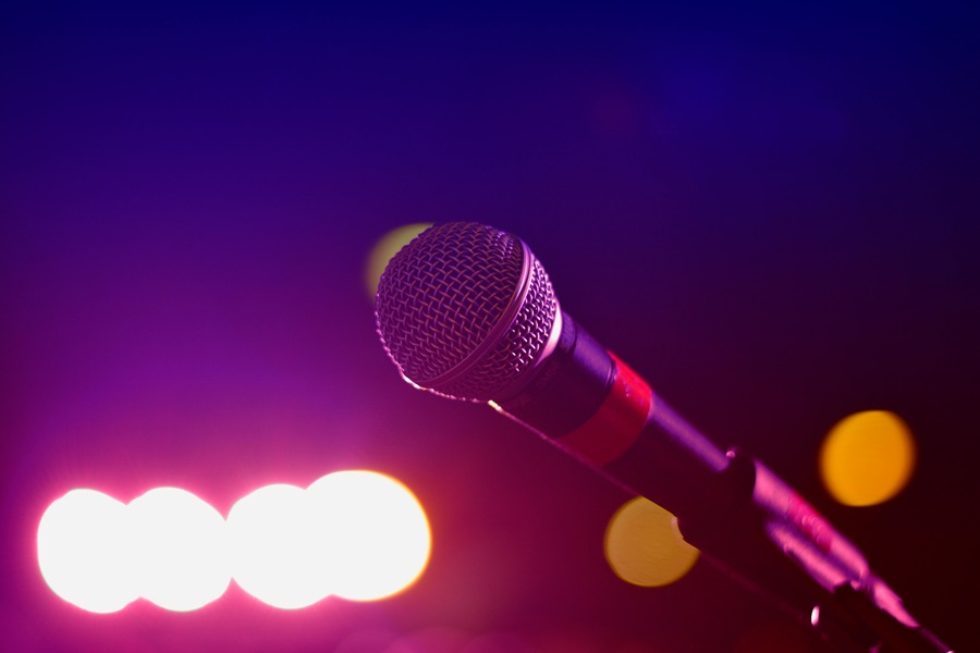10 Songs to Listen to When you Want to Make a Deal Close Up of a Mic on a Stand with Blurred Lights in the Background