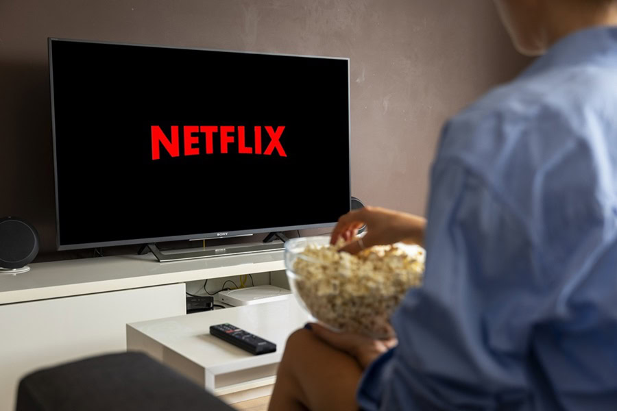 Netflix Shows to Watch After a Long Day at Work View of a TV with Netflix on the Screen from Over the Shoulder of a Person Eating Popcorn from a Glass Bowl