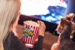 Netflix Shows to Watch After a Long Day at Work a Woman Eating Popcorn From a Small Popcorn Bucket with a TV in the Background