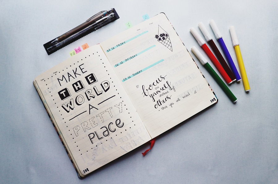 Benefits of Bullet Journaling Overhead View of a Bullet Journal That Says Make The World a Better Place with Pens on Each Side