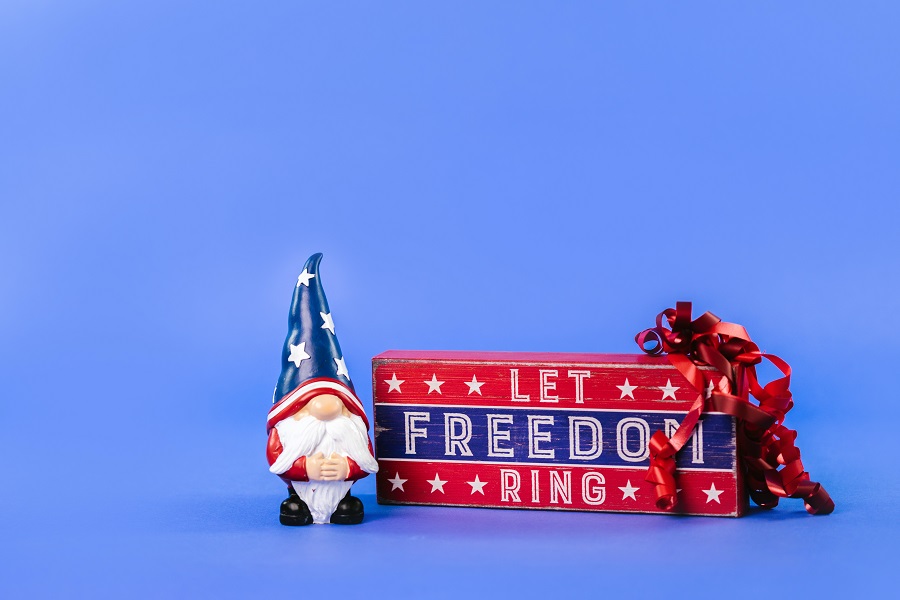 July 4th Decorations a Wodden Sign That Says "Let Freedom Ring" Next to a Toy Gnome with an American Flag Hat