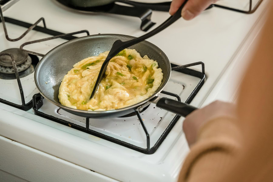 Clean Eating Breakfast Recipes Close Up of a Person Cooking Eggs in a Small Frying Pan on a Gas Stove