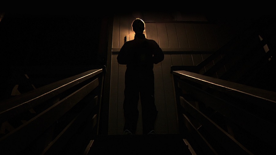 Scary Netflix Movies Man Standing Outside of a Door with a Light Shining Behind Him Making it Hard to See his Features