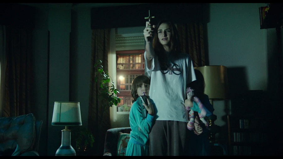 Scary Netflix Movies Teenage Girl Standing in a Room with Her Younger Siblings Holding a Crucifix Out