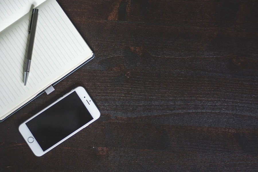 15 iPhone Wallpapers to Inspire Anyone an iPhone Next to a Notepad on a Wooden Surface