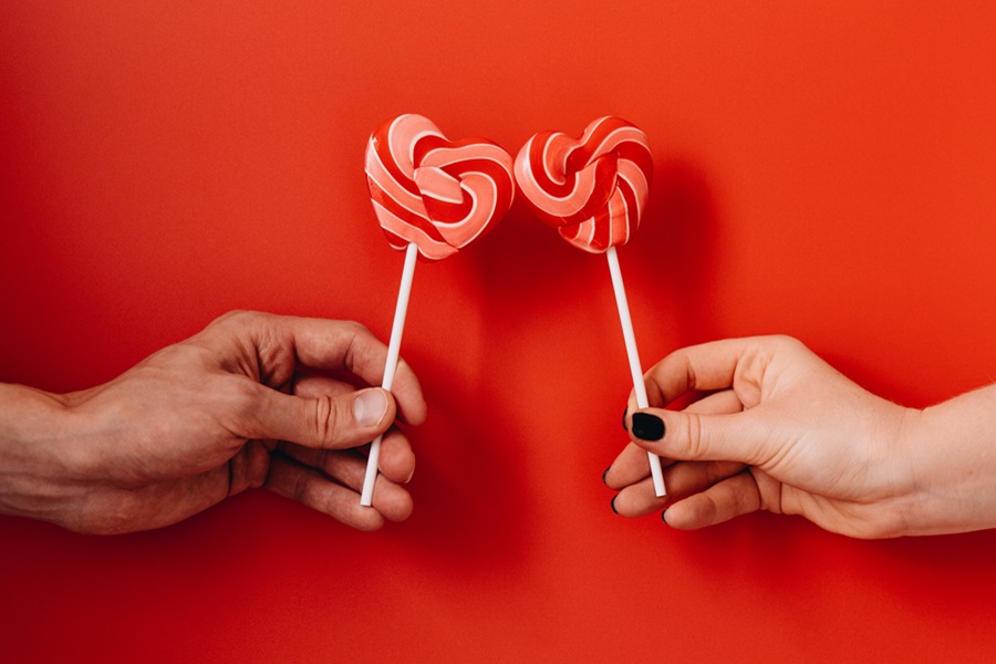 Sexy Valentine's Day Nail Ideas Close Up of Two People's Hands Each Holding Out a Heart-Shaped Lollipop