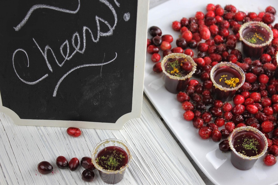 How to Make Cranberry Jello Shots a Platter of Cranberries with Cranberry Jello Shots and a Chalkboard Sign that Reads Cheers!