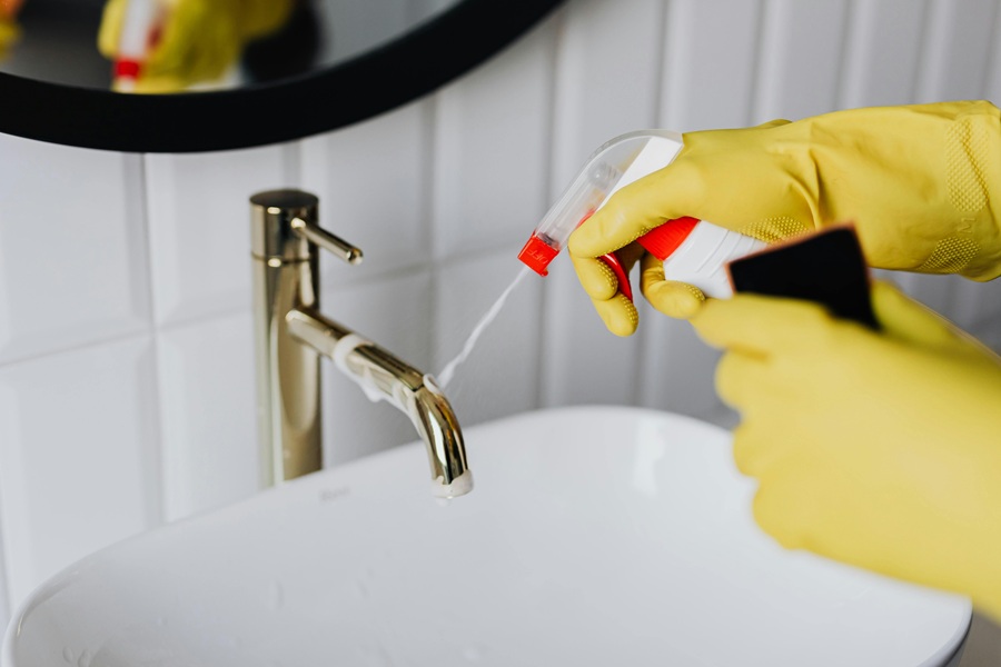 Hydrogen Peroxide Cleaner DIY Recipes a Person Spraying a Cleaner on a Faucet Above a Sink