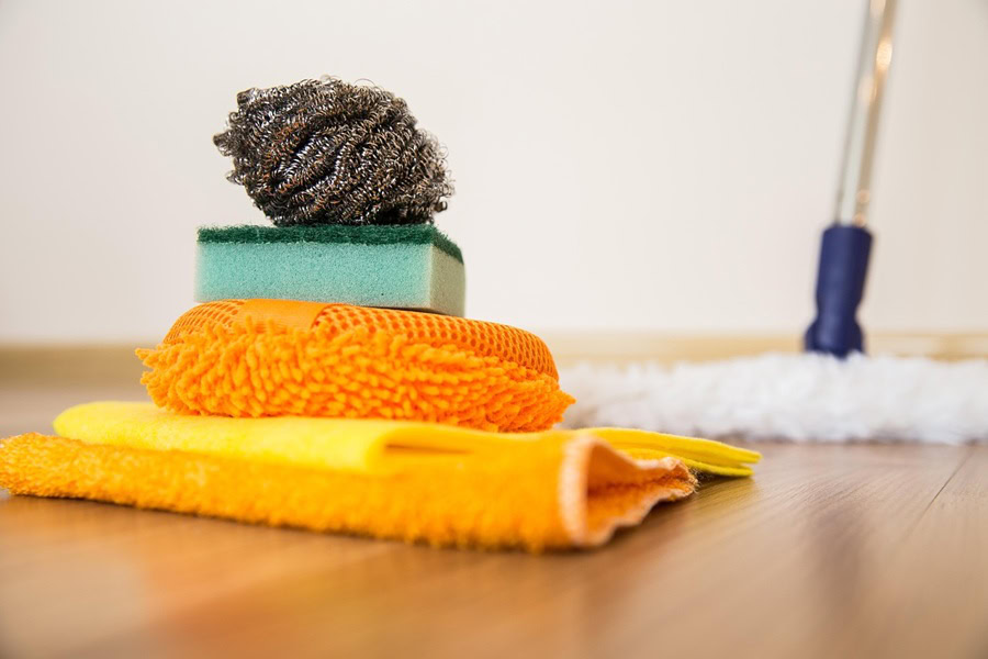 Hydrogen Peroxide Cleaner DIY Recipes a Stack of Cleaning Towels, a Sponge, and a Duster on a Hardwood Floor