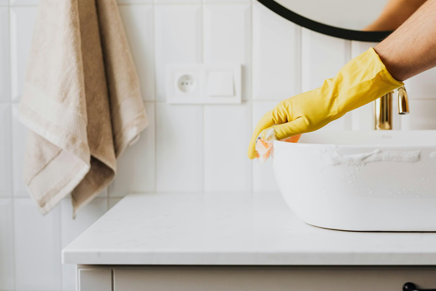 Hydrogen Peroxide Cleaner DIY Recipes Close Up of a Person Cleaning a Sink Wearing Yellow Rubber Gloves