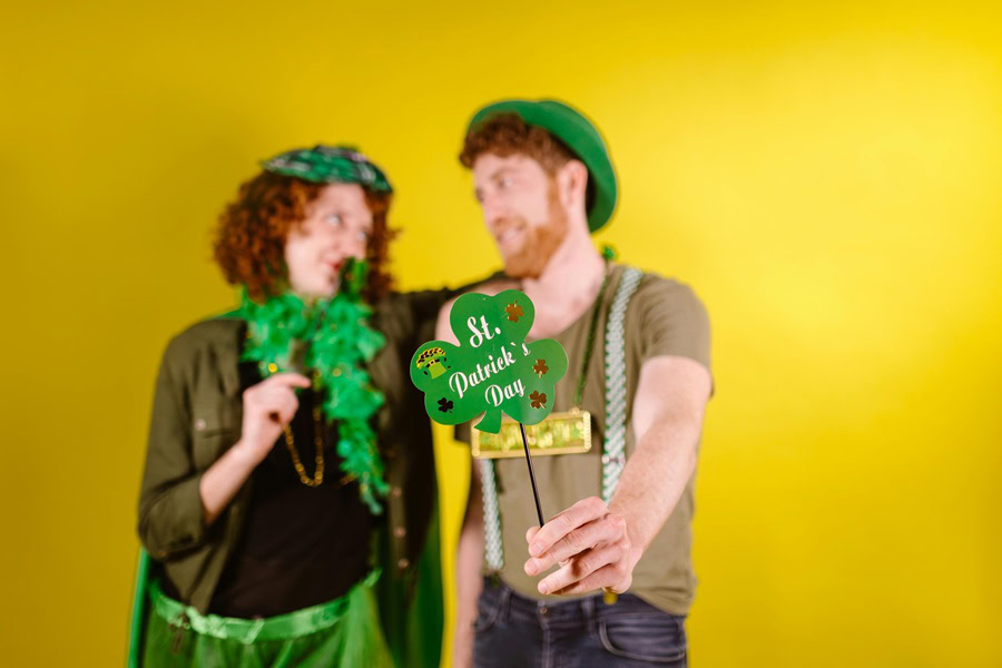 Leprechaun Trap Ideas Two People Standing In Front of a Yellow Wall Holding St. Patrick's Day Signs and Wearing St. Patrick's Day Hats