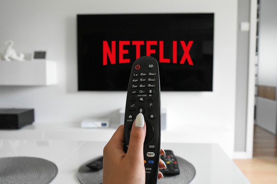 Best Netflix Series for Teens Close Up of a Person Holding a Remote Control Up with a TV in the Background with Netflix on the Screen