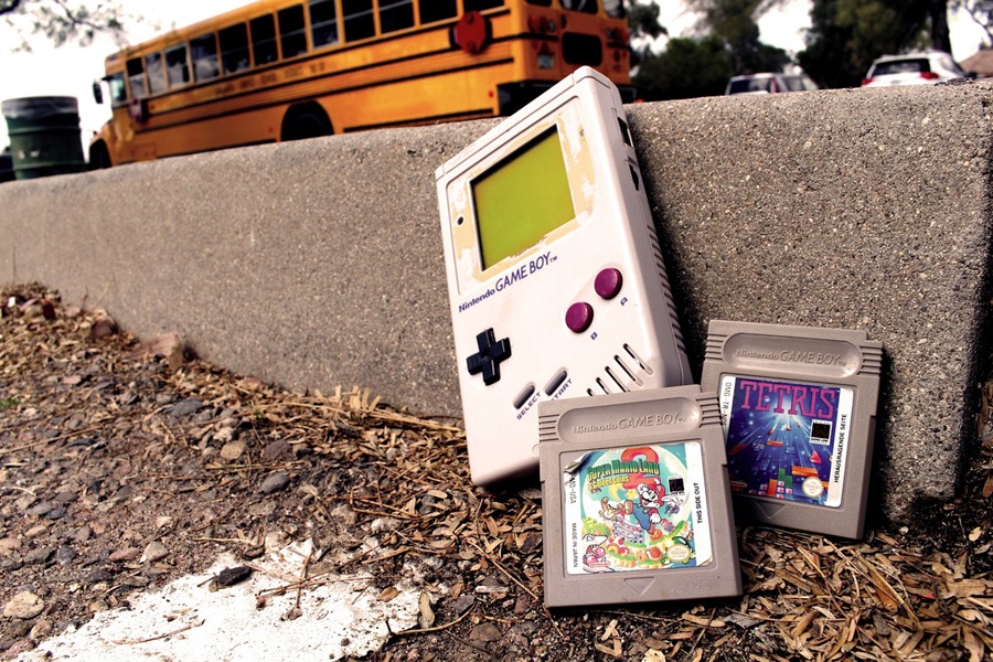 Best Netflix Series for Teens a Gameboy and Two Games Resting Against a Curb Outside a School with a School Bus in the Background