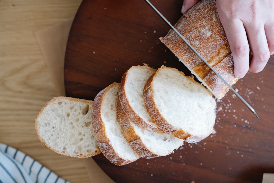 Gluten Free Bread Machine Recipes to Bake a Loaf of Bread on a Wooden Cutting Board Being Sliced by a Person