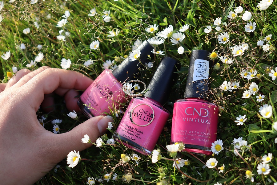 Red White and Blue Nails  Nail Polish Lying on Grass  with a Woman's Hand Holding One Bottle of Polish