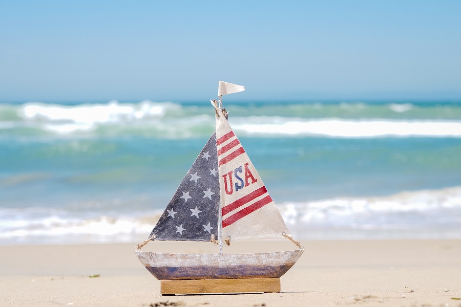 Fourth of July Facts to Know Close Up of a Small Wooden Boat Toy with an American Flag Sail on a Beach