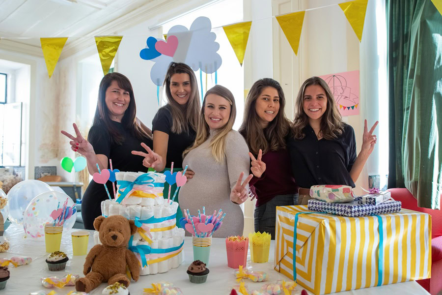 Baby Shower Ideas for Boys a Group of Women Posing Behind a Table with Party Decor Behind Them and Diaper Towers, Gift Bags, and a Baby Shower Cake on a Table
