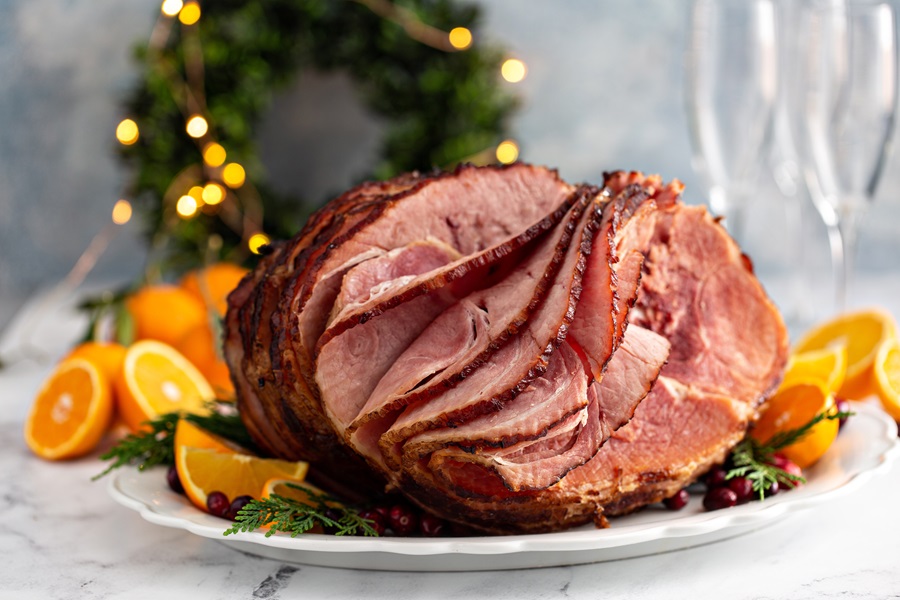 How to Cook A Ham Like A Pro Close Up of a Christmas Ham Sliced to Serve with Christmas Decorations in the Background