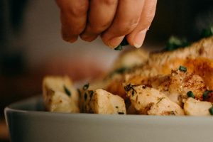 Best Thanksgiving Stuffing Recipes Close Up of a person's hands Sprinkling Seasoning on Bread Chunks in a Baking Dish