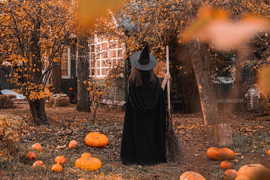 Halloween Cocktails with Whiskey a Witch Walking Up to a House with Pumpkins Scattered Around the Lawn