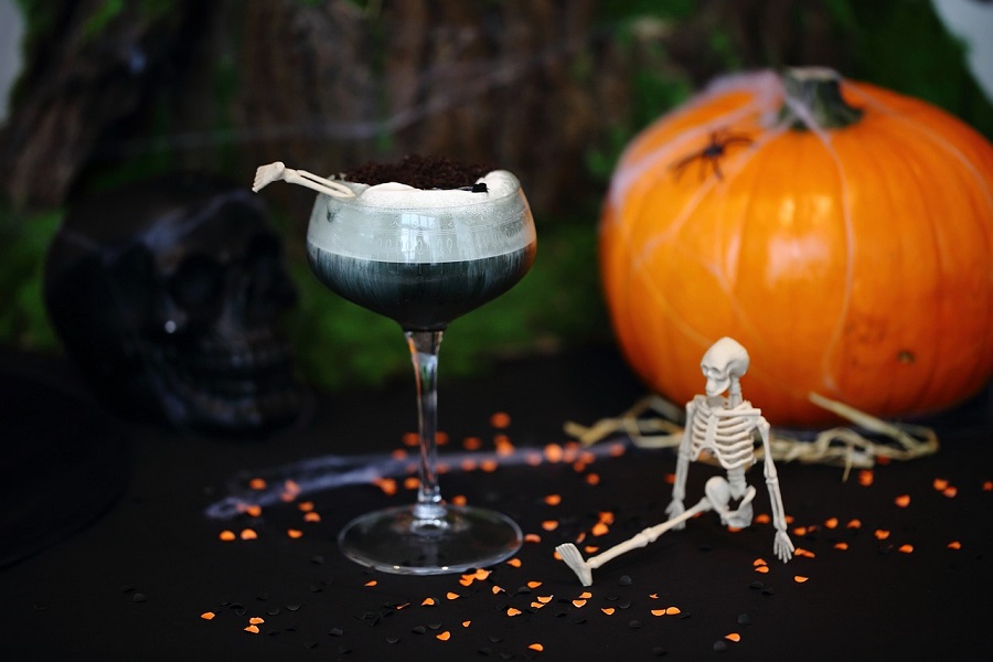 Halloween Cocktails with Whiskey a Black Cocktail on a Table Next to a Pumpkin and a Small Toy Skeleton