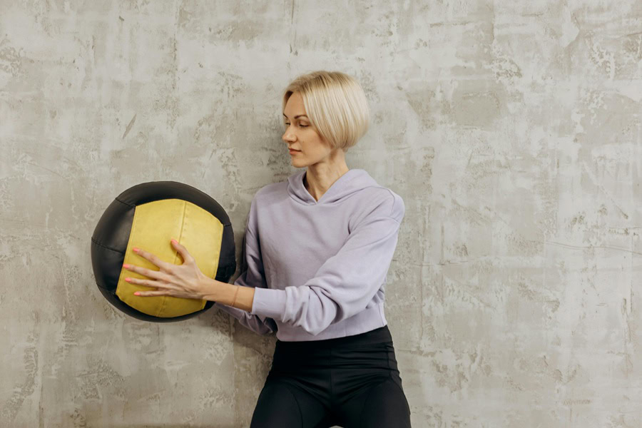 Muffin Top Workouts a Woman Standing Against a Wall Holding a Medicine Ball