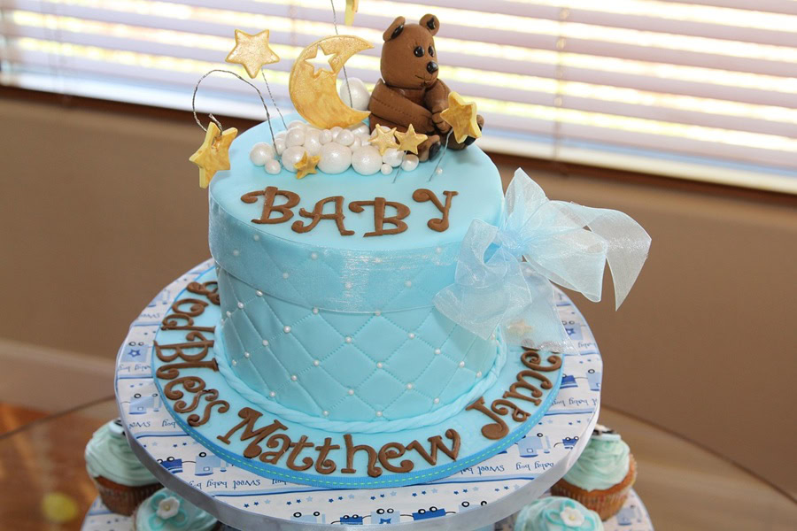 Baby Shower Cakes for Boys a Tall Cake with Blue Icing and Baby Written on Top in Brown with a Teddy Bear and Moon Made from Fondant