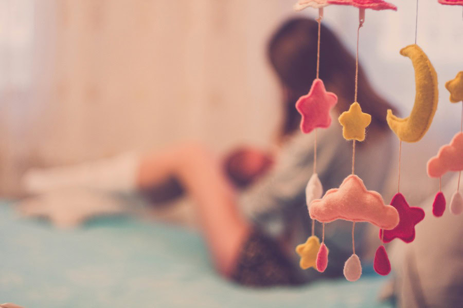 Baby Shower Ideas for Girls  Close Up of a Pink and Brown Mobile with a Blurred View of a Mom Holding a  Baby