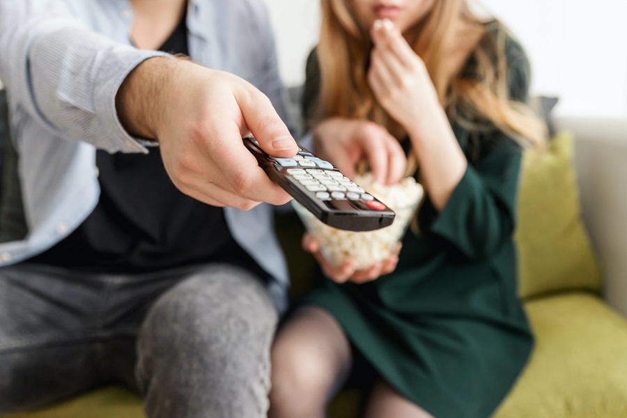 Netflix Shows to Binge Watch as a Couple Close Up of a Man Holding a Remote Control Toward the TV with a Woman Sitting Next to Him