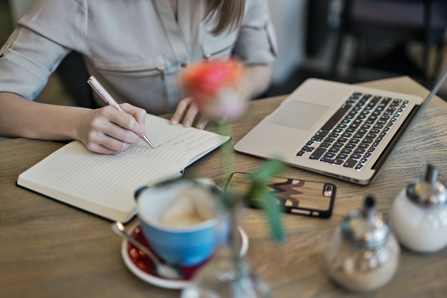 How to Set up your Bullet Journal for the New Year Close Up of a Woman Writing in a Bullet Journal on a Desk Next to a Laptop