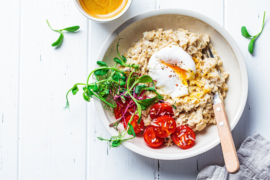 Savory Oatmeal Recipes Savory oatmeal with poached egg, tomatoes, cheese and sprouts in a white bowl. Healthy breakfast concept.