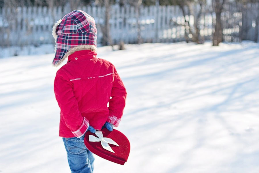 Fun and Free Valentine's Day Printables for Kids a Little Boy Walking in Snow Holding a Heart-Shaped Box of Chocolates Behind His Back