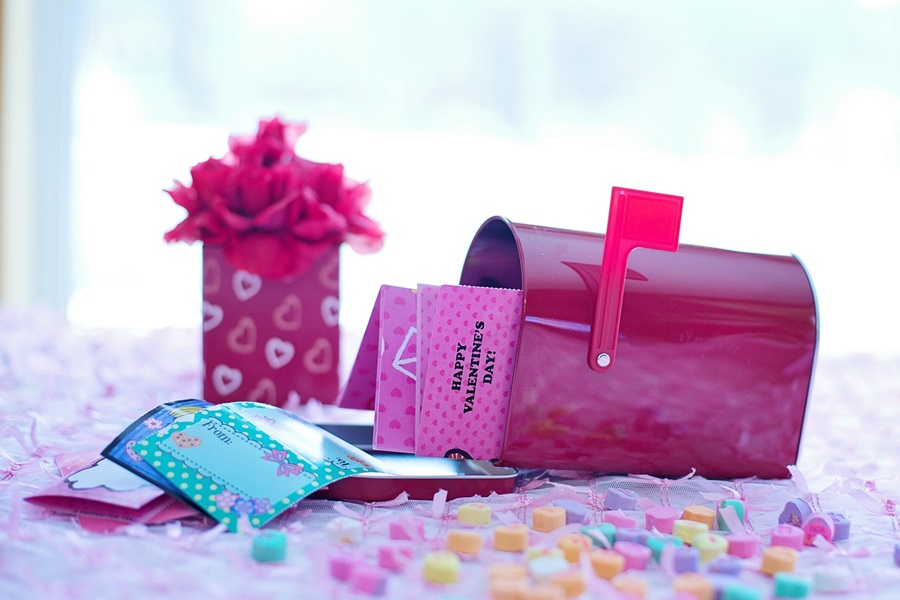 Fun and Free Valentine's Day Printables for Kids a Pink Mailbox Opened with Letters Sticking Out Next to a Vase of Flowers and Conversation Heart Candies Scattered Around
