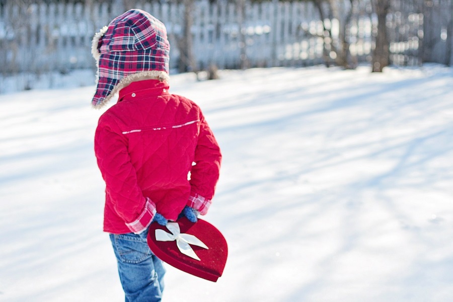 Funny Valentines Quotes Boy Wearing Red Walking Through Snow Holding a Heart Shaped Box Behind His Back