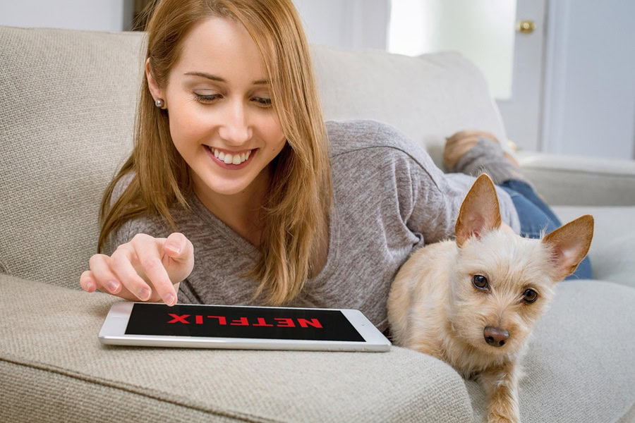 Netflix Shows Best Shows to Watch for All Ages a Woman Sitting on a Couch with a Puppy Watching Netflix on a Tablet