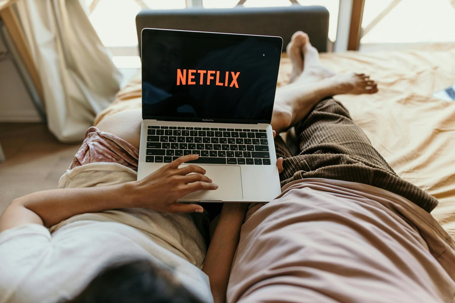 Netflix Shows Best Shows to Watch for All Ages a Couple Laying Down on a Bed Watching Netflix on a Laptop