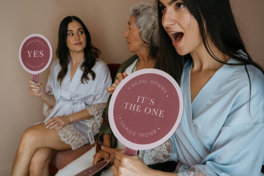 Bridal Shower Brunch Games Three Women Sitting Down Looking at Something Off Camera, Smiling and Holding Signs That Say The One.