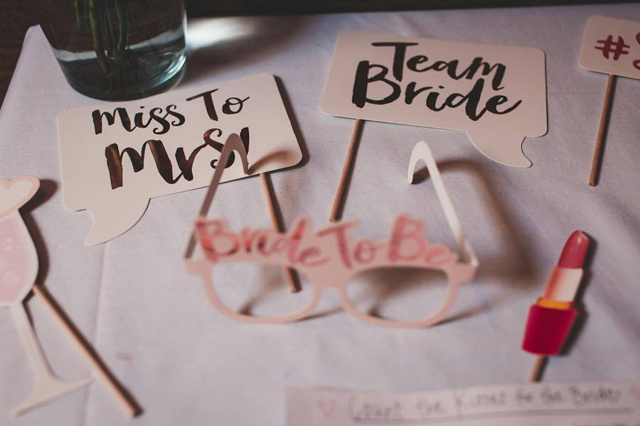 Bridal Shower Brunch Games Close Up of a Pair of Glasses That Say Bride to Be on them On a Table with Two Small Pieces of Paper that Say Miss to Mrs. and Team Bride