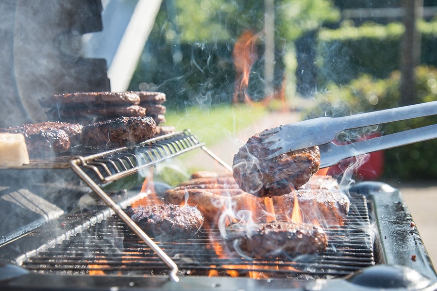 15 Backyard BBQ Drinks for an Outdoor Party View of a BBQ Grill with a Person Using Metal Tongs to Flip Burger Patties