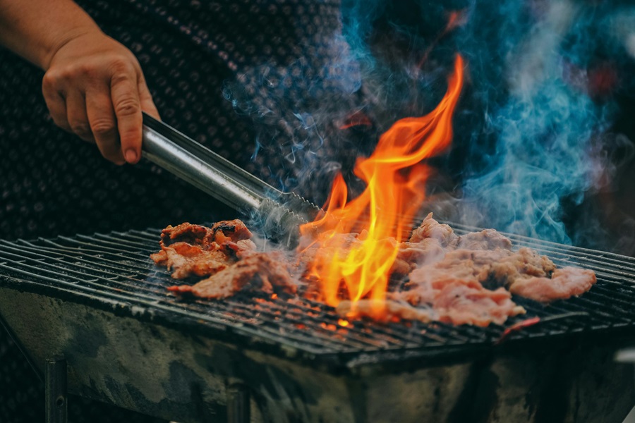 Best Side Dishes for a BBQ Delicious Cookout Recipes Close Up of a Grill with Fire Coming From Underneath, Meat on the Grill and a Person Holding Tongs Close to the Meat