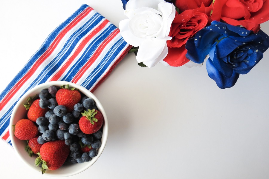 July 4th Recipes Overhead View of a Bowl of Mixed berries Next to a Bouquet of Patriotic Flowers and a Red, White, and Blue Striped Towel