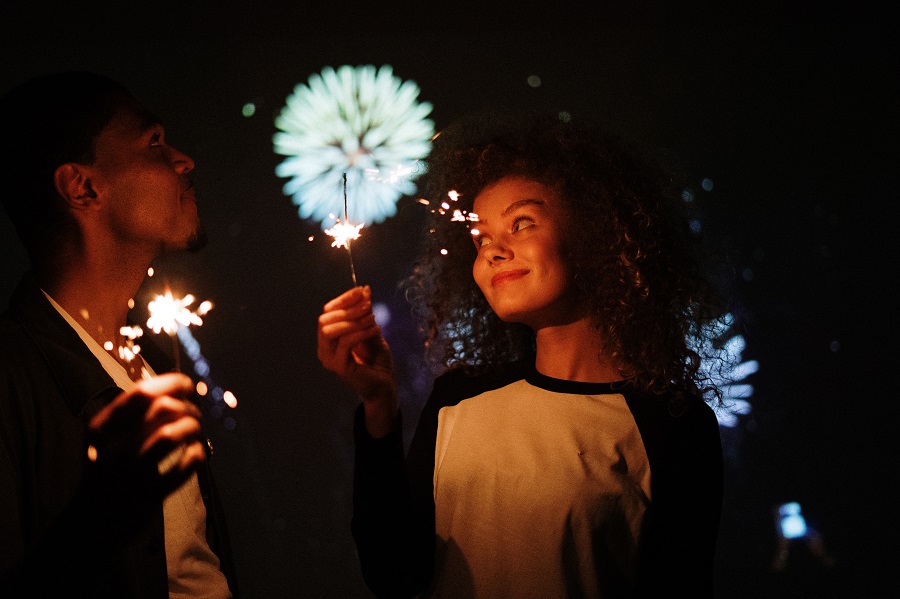 4th of July Instagram Captions a Man and a Woman Hold Small Sparklers at Night While Fireworks go Off Behind Them