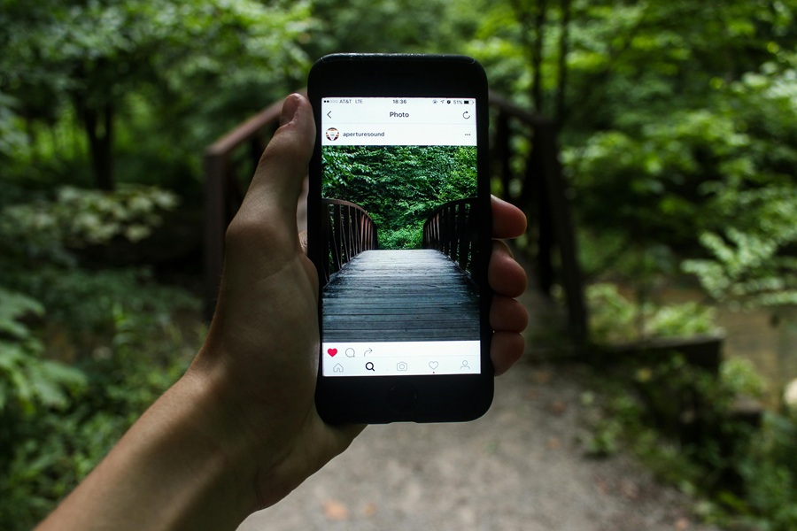 Motivational Instagram Captions Close Up of Instagram open on a Phone Being Held Up by a Person's Hand with a Hiking Trail in the Background