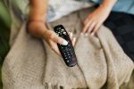 Best Feel Good Movies on Amazon Prime Close Up of a Remote Control in a Person's Hand Resting on a Blanket on Their Lap