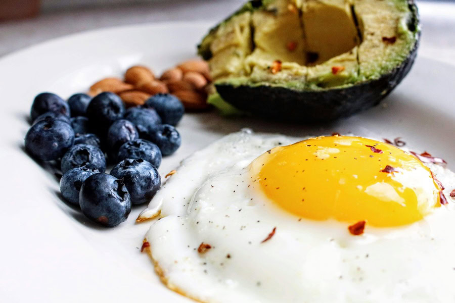 Clean Eating Tips for Beginners a Cooked Egg, Half an Avocado, and Blueberries on a Plate