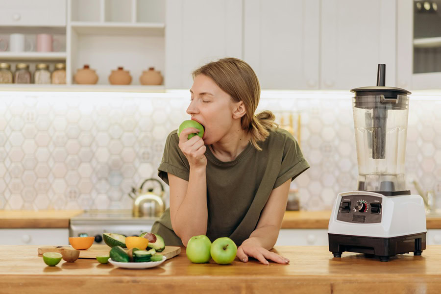 Clean Eating Tips for Beginners a Woman Eating an Apple in a Kitchen