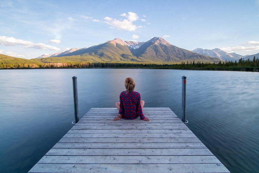 Quotes for National Relaxation Day #NationalRelaxationDay Woman Sitting on a Dock on a Lake with Mountains Straight Ahead