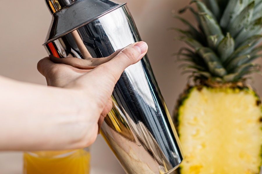 Banana Creme Rum and Orange Juice Cocktail Close Up of Someone's Hand Holding a Cocktail Shaker with a Pineapple in the Background