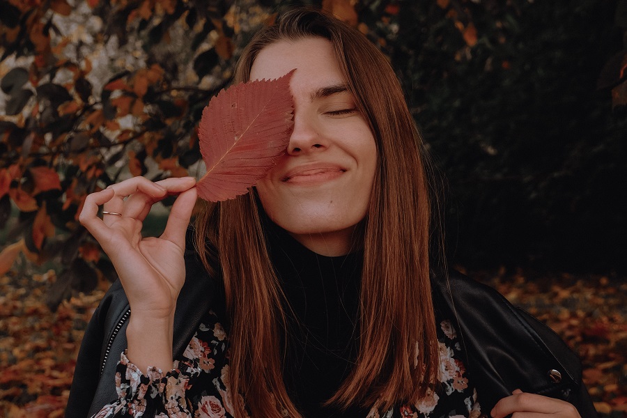 Fall Nail Designs a Woman Smiling and Holding a Fall Leaf in Front of One Eye